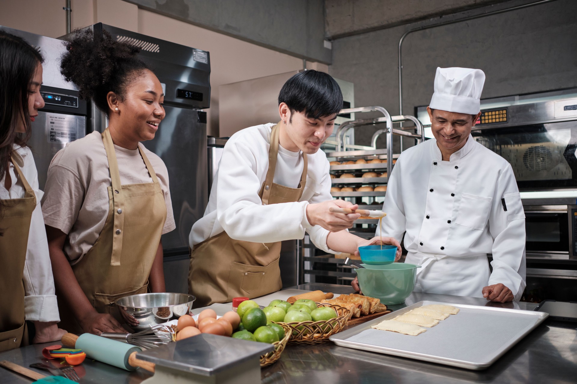 Senior chef teaches cooking students to prepare pastry dough for fruit pies.